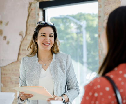 The mid adult female real estate agent smiles at the unrecognizable female customer.
